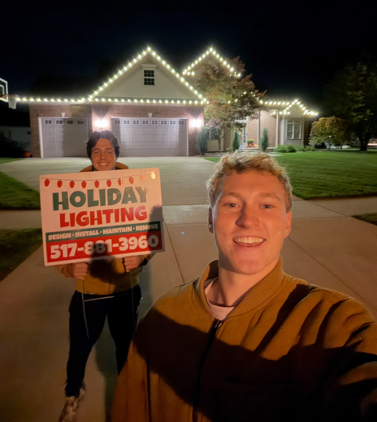 Graham and Kennan, owners of Greater Lansing Holiday Lighting, in front of a freshly lit home