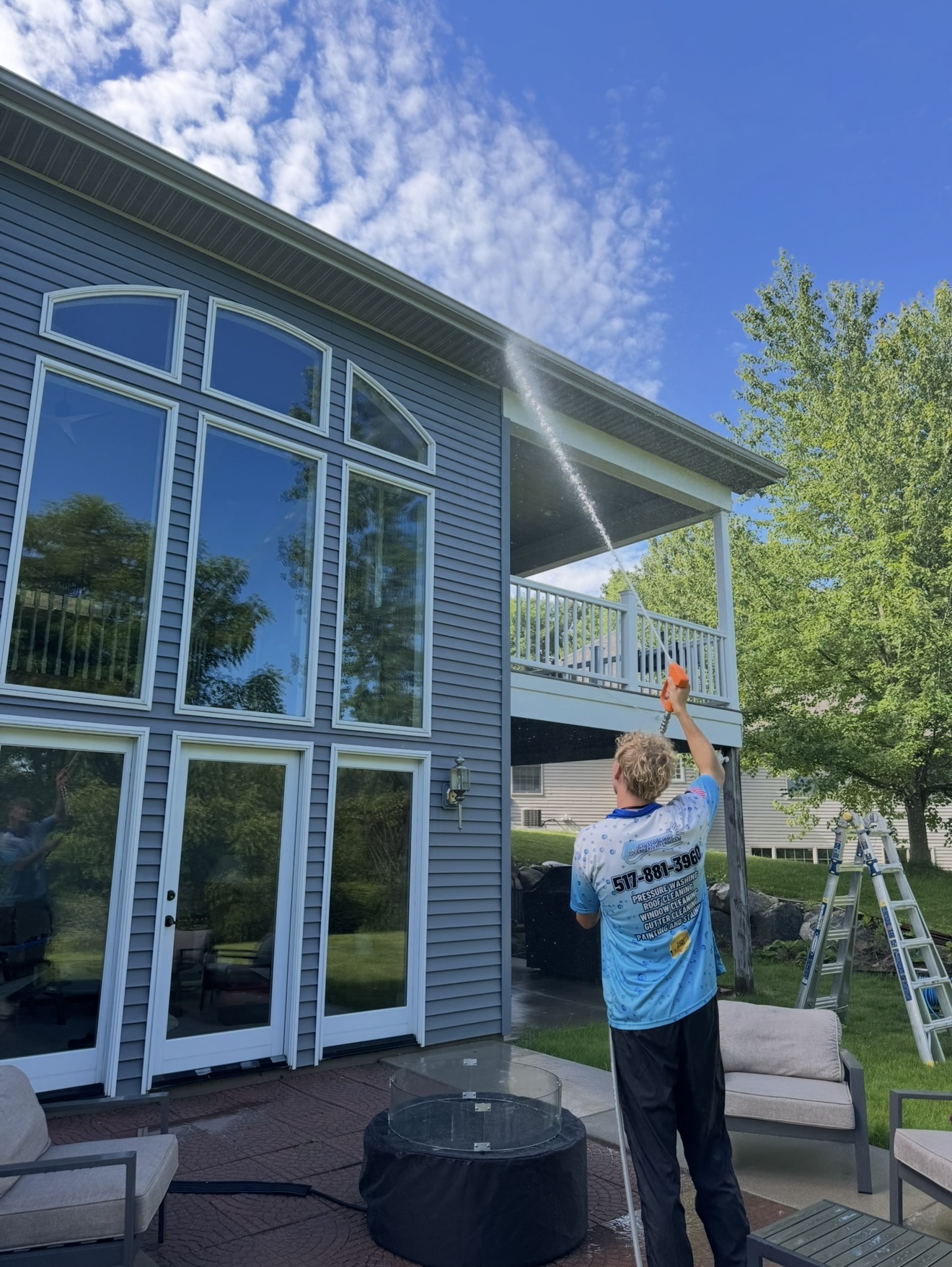 Graham pressure washing the siding and windows of a Greater Lansing home on a summer day