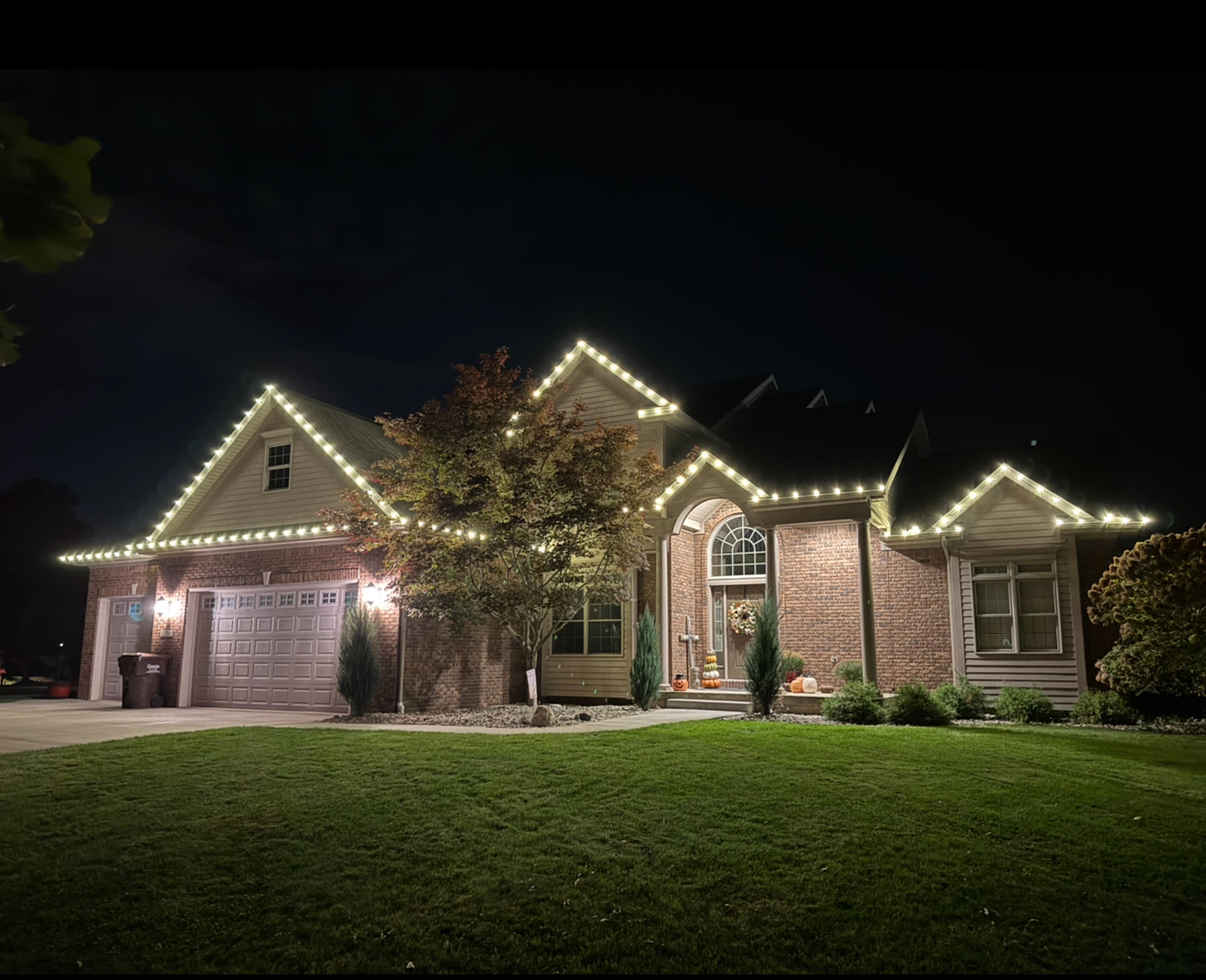 Brick home in Okemos at dusk with warm white holiday lights outlining every roof peak